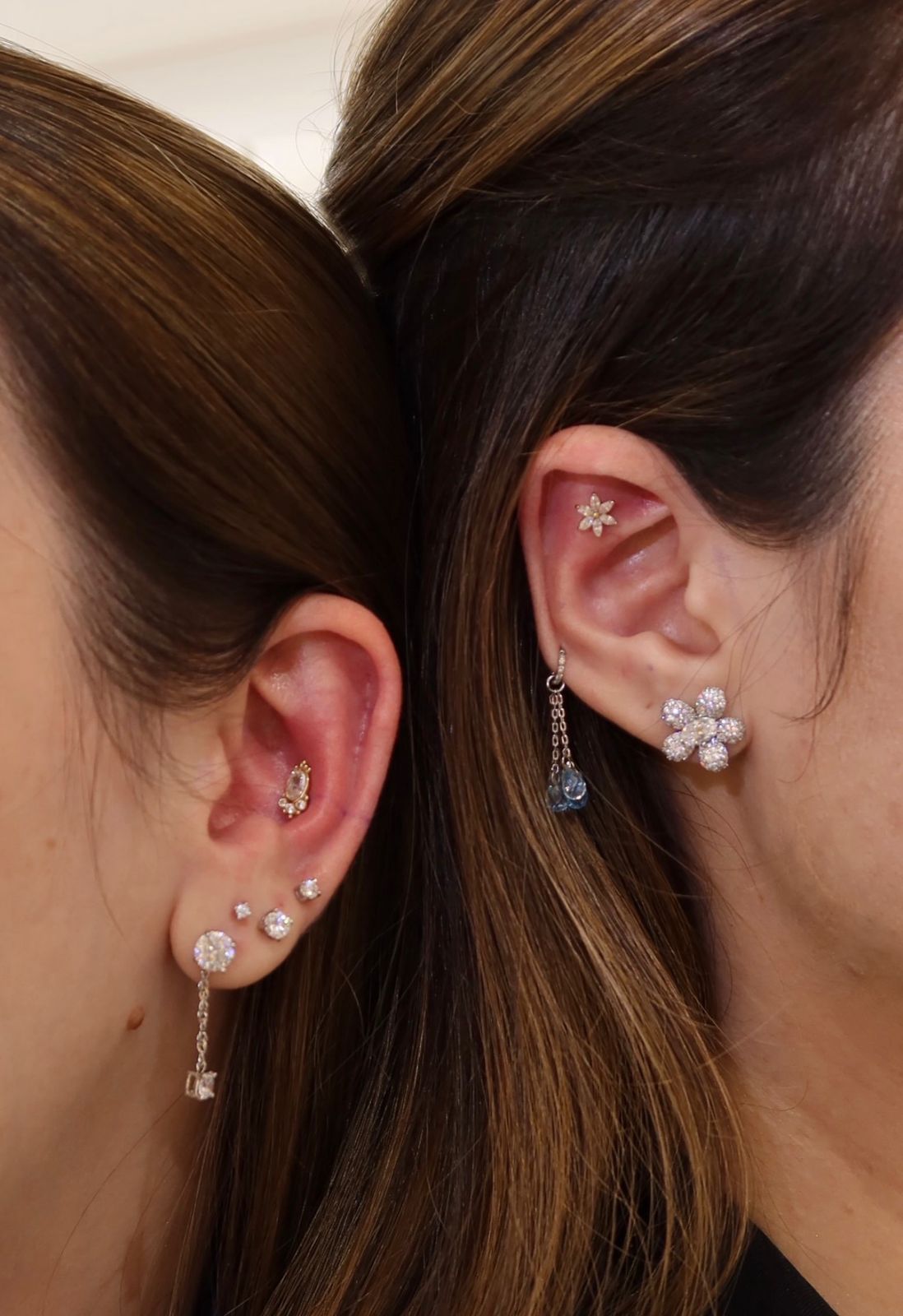 Duas orelhas com múltiplos piercings delicados em ouro e brilhantes, trabalho de body piercing na Maria Antonieta
